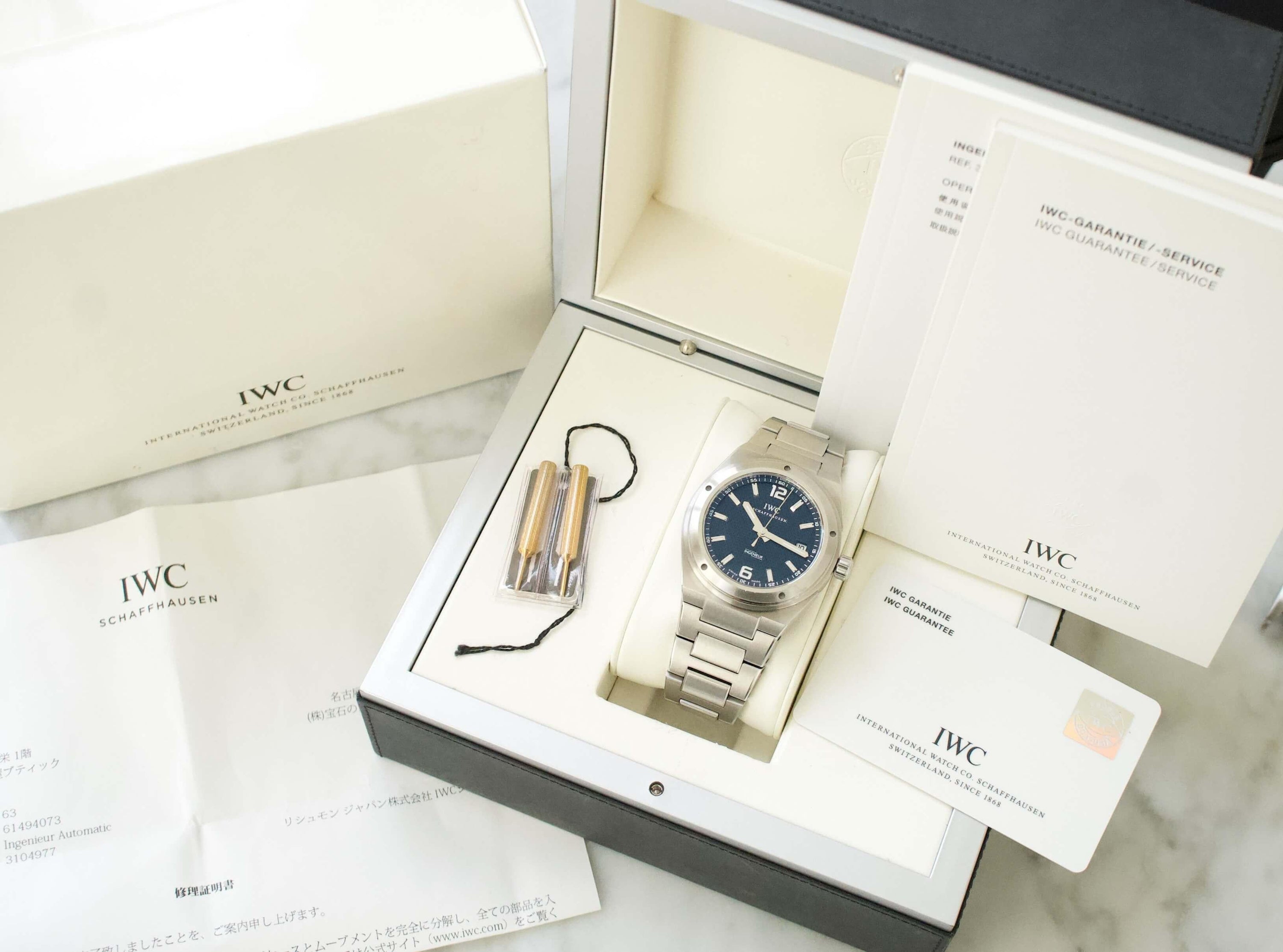 Stainless steel IWC luxury watch with blue dial in original box, shown with warranty cards and documents.