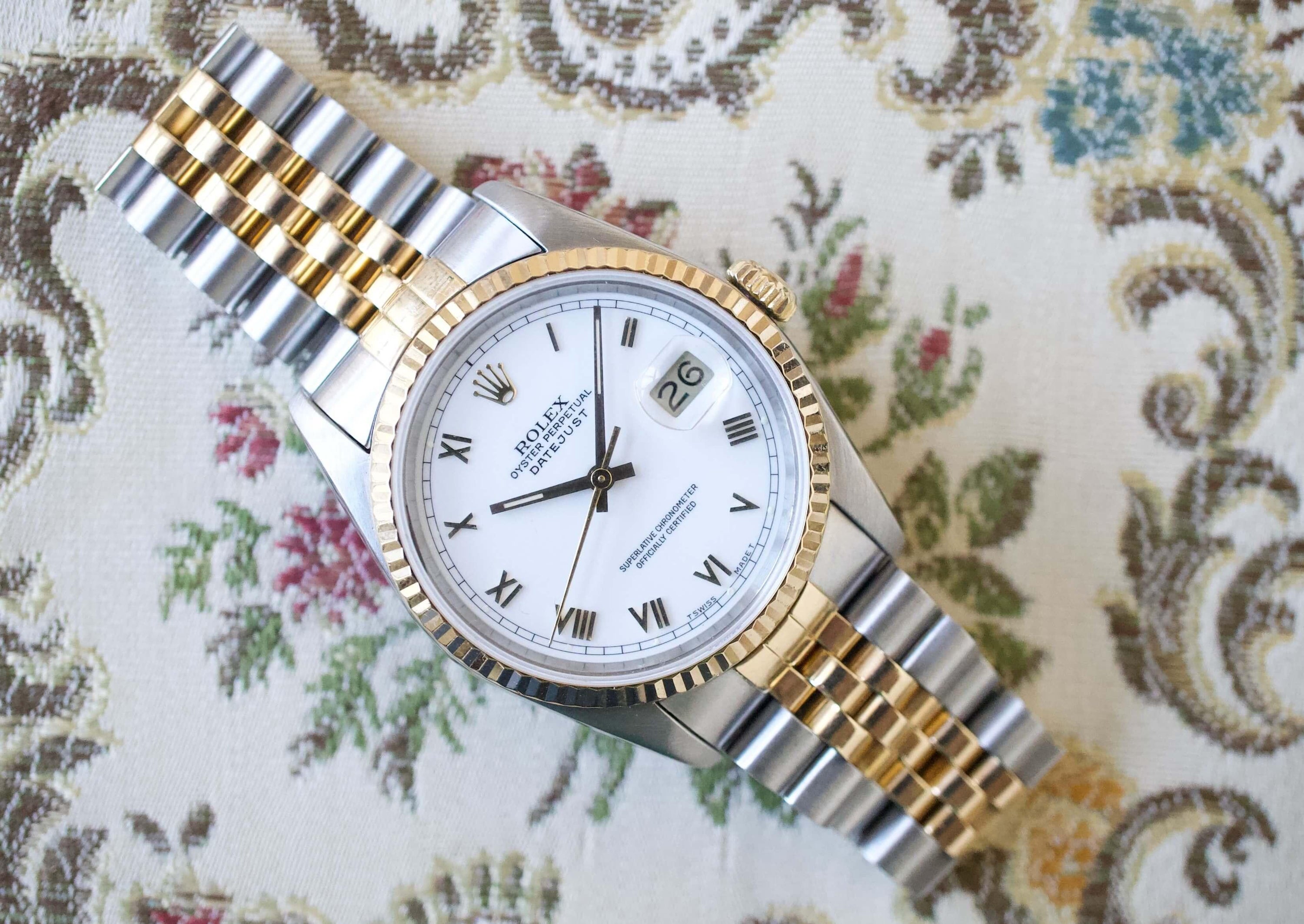 Two-tone luxury watch with Roman numerals and date display on a floral background