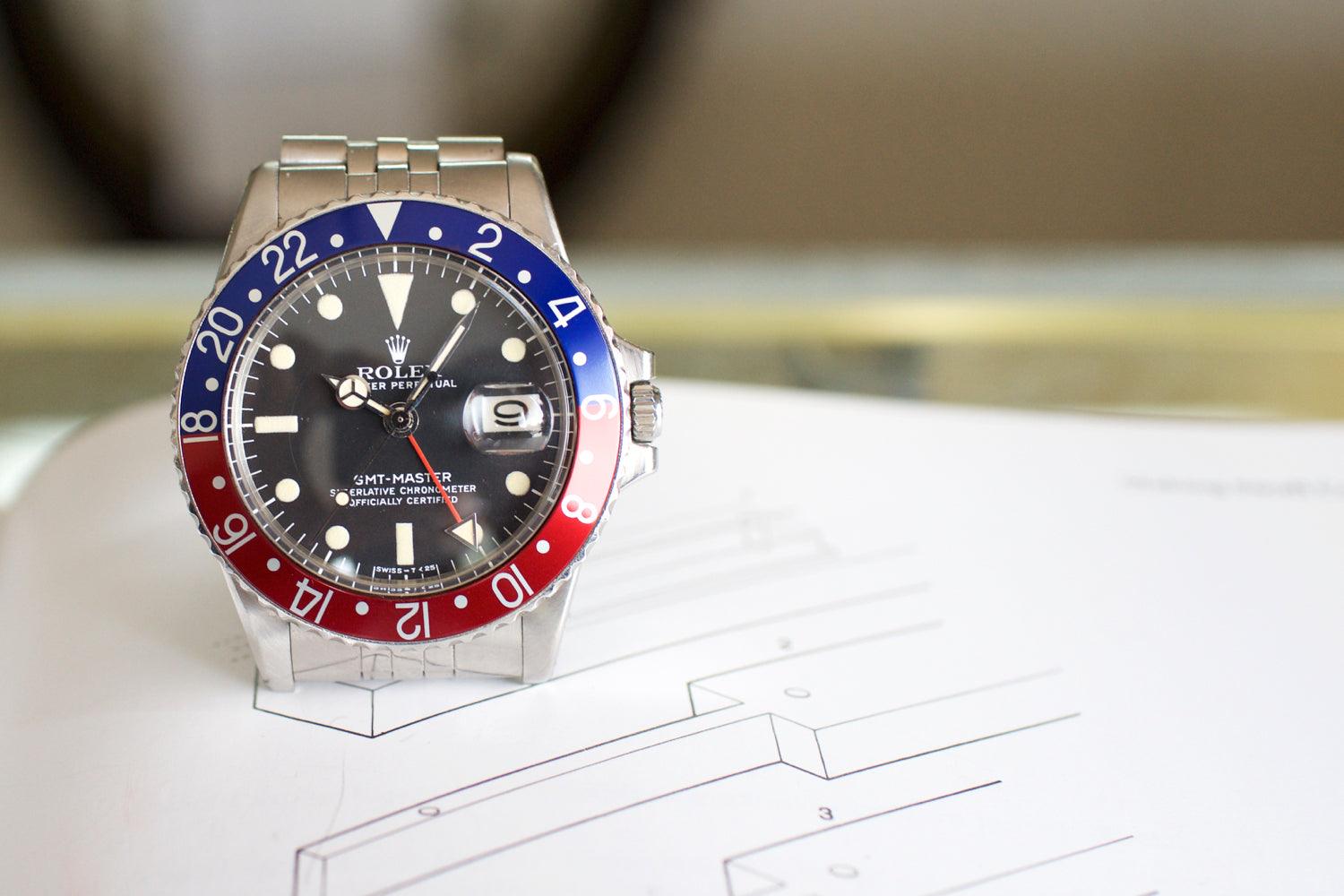 Vintage stainless steel GMT watch with red and blue bezel on a document background
