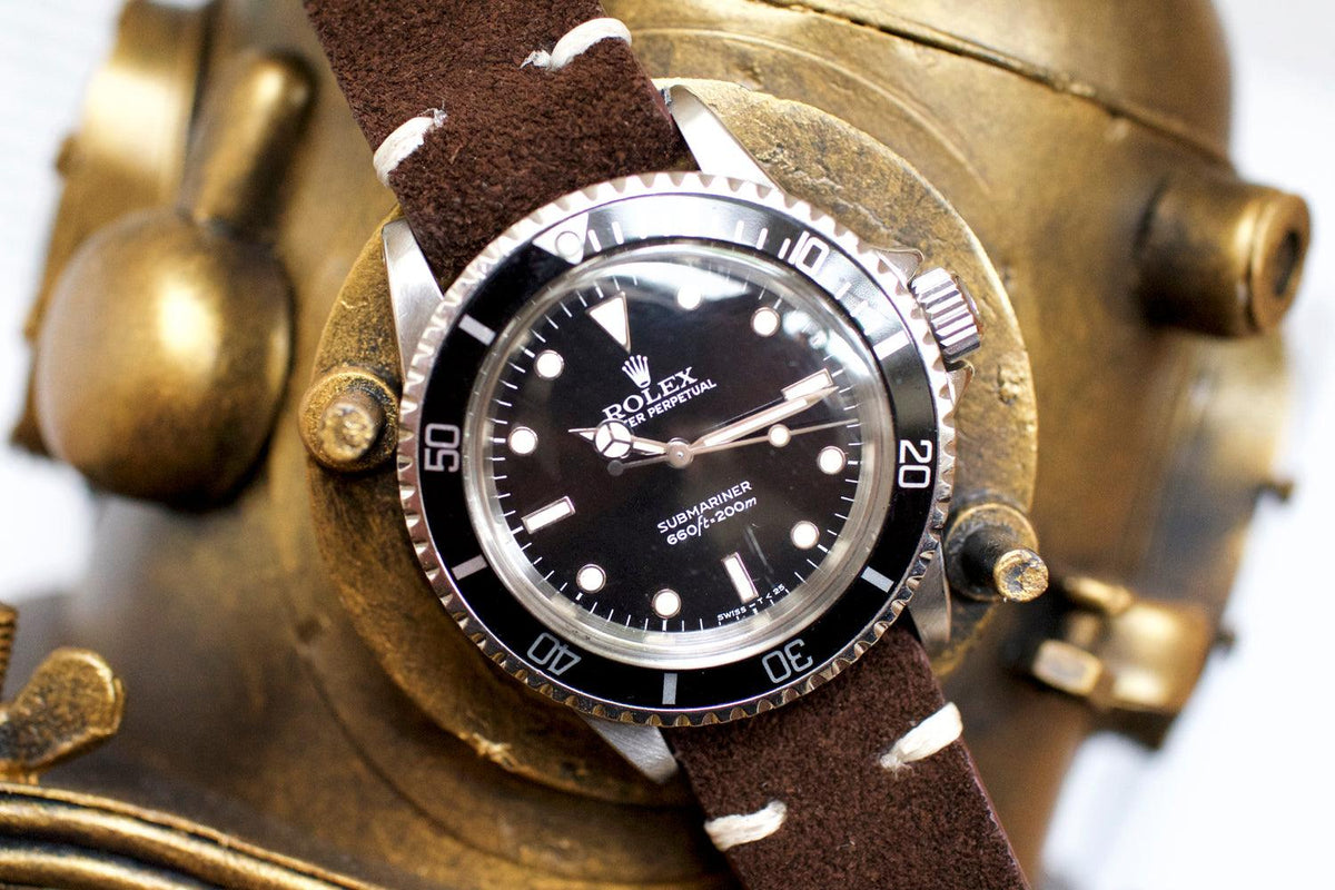 Vintage black dial luxury dive watch on brown suede strap, displayed on brass helmet