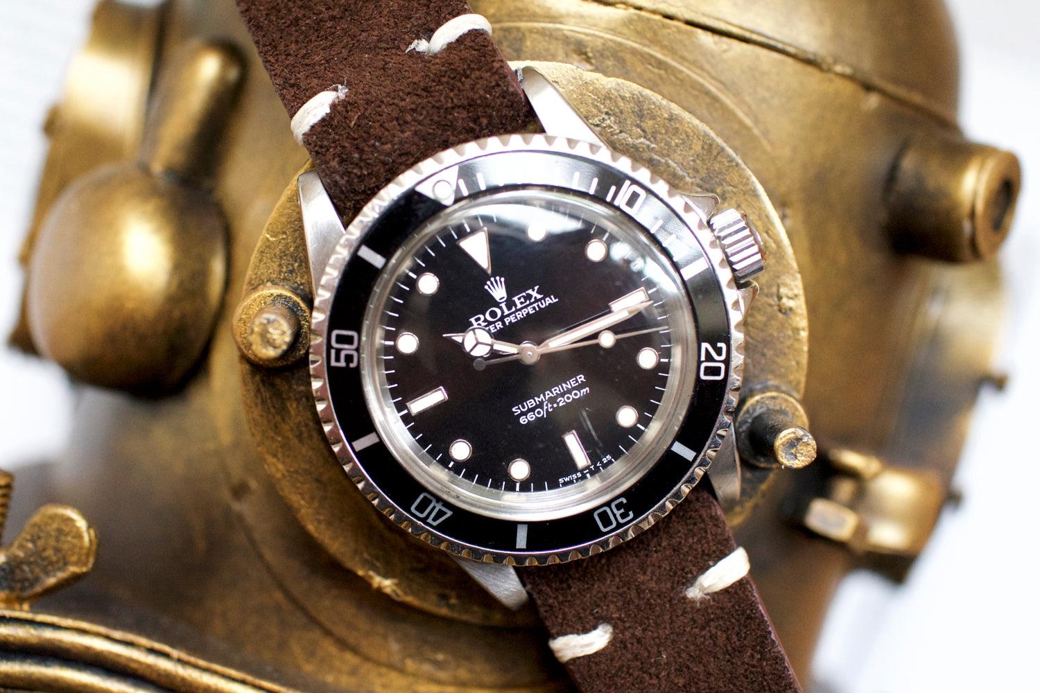 Vintage black dial luxury dive watch on brown suede strap, displayed on brass helmet