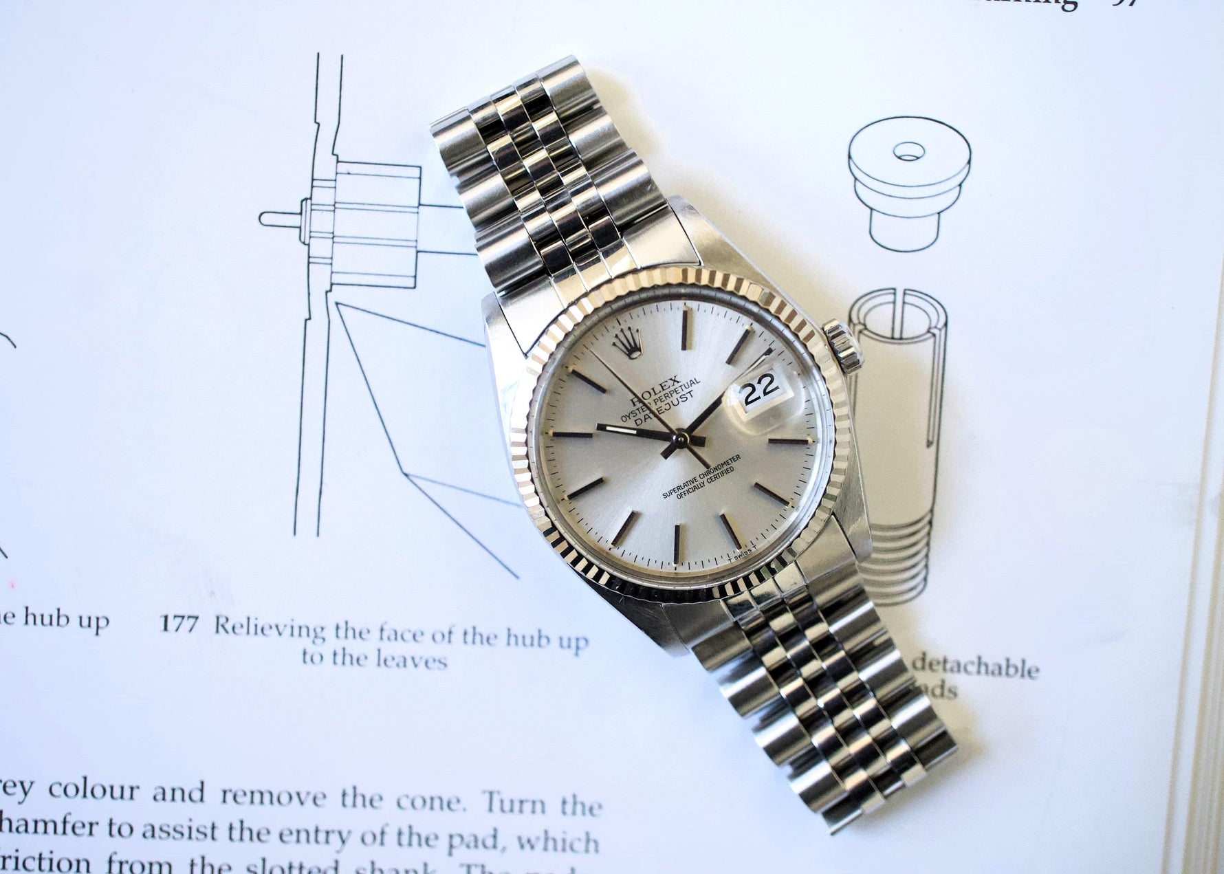Stainless steel Swiss luxury watch with silver dial and date display on technical drawings