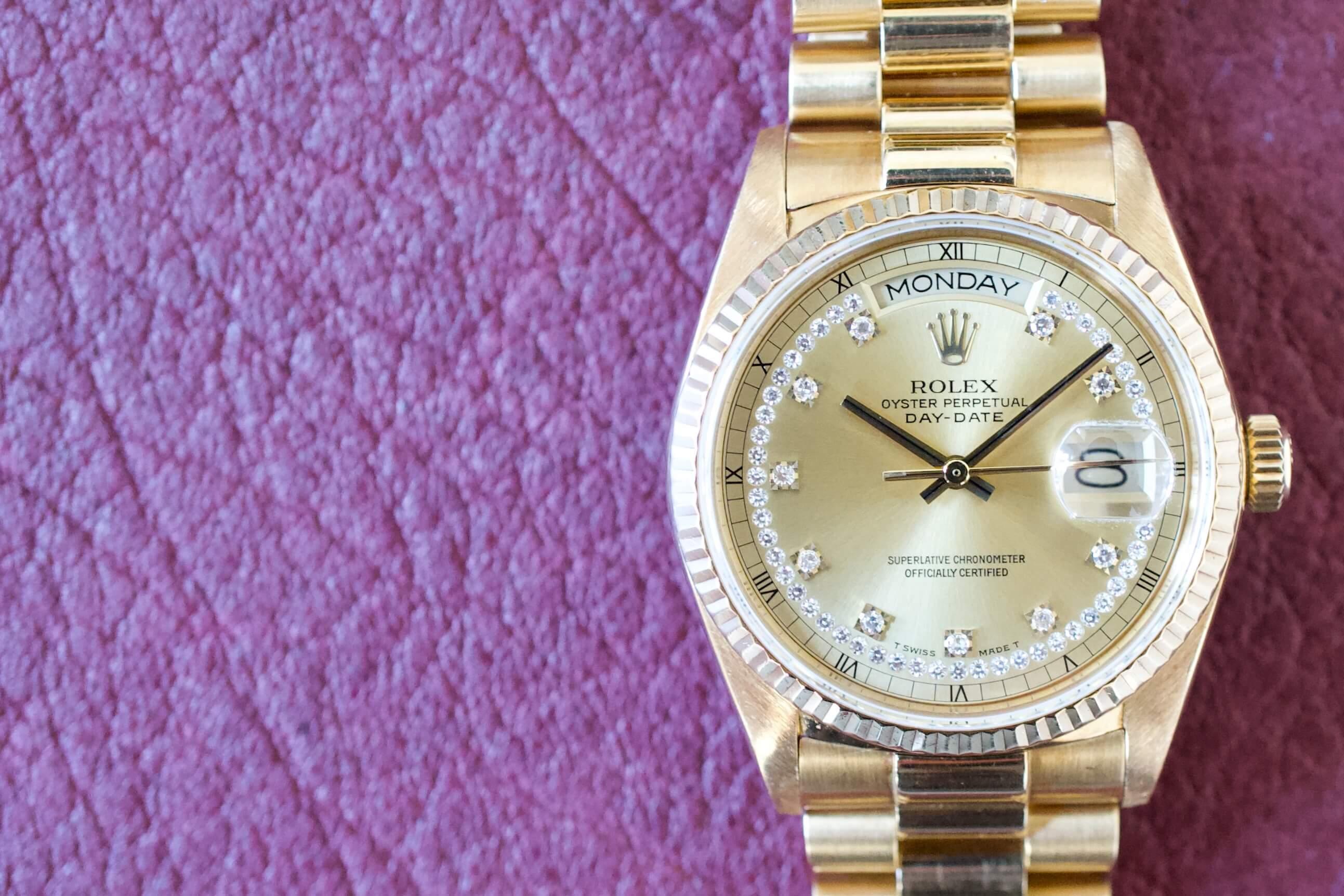 Gold luxury watch with diamond dial and day-date display on a purple textured surface