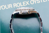 Side view of a luxury Rolex watch with a silver band against a green background