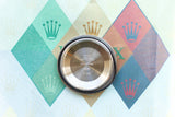 Back of a stainless steel Rolex watch case resting on a colorful branded background.