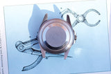 Rear view of a luxury stainless steel watch case resting on a blue technical drawing.