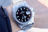 Close-up of a Rolex Explorer II luxury watch with a black dial and steel bracelet on a wrist.