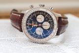 Luxury chronograph watch with blue dial, silver case, and brown leather strap on open book