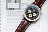 Men's chronograph luxury watch with black dial and brown leather strap on open magazine