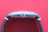 Side view of a luxury watch case with a crown and strap against a red background