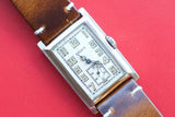Vintage Gruen rectangular watch with a brown leather strap on a red background