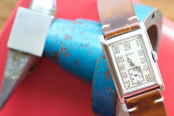 Vintage Gruen rectangular watch with brown leather strap resting on a blue metal tool.