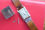 Vintage Gruen rectangular watch with brown leather strap and watch tools on red surface