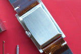 Close-up of the brushed stainless steel case back of a rectangular luxury watch with leather strap