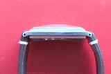 Side view of a luxury watch with a rectangular silver case and black leather strap