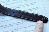 Close-up of a brown leather luxury watch strap with white stitching on a text background.
