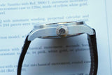 Side profile of a luxury silver watch with a knurled crown and black leather strap.