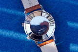 Case back of a Memovox luxury watch with a brown leather strap on a blue background
