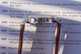Side view of a luxury watch with a brown leather strap over a historical text document.