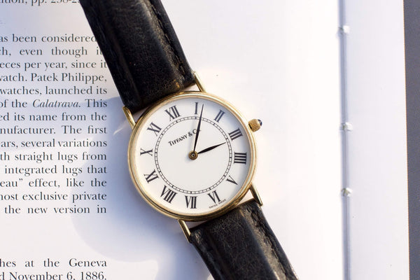Tiffany & Co. luxury gold watch with Roman numerals and black leather strap on a book page
