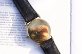 Back view of a 14K gold Tissot watch with a black leather strap on a book page.