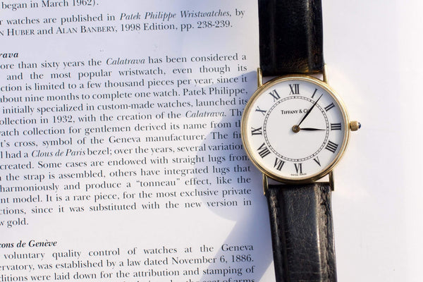 Tiffany & Co. luxury gold wrist watch with black leather strap resting on a book page.