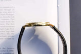 Side view of a luxury gold watch with a black leather strap resting on a white book page