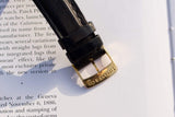 Close-up of a black leather watch strap with a gold Tiffany & Co. buckle on a book page.