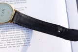 Back of a luxury Swiss-made gold watch with a black leather Tiffany strap on a page of text.