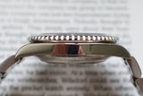 Side profile of stainless steel luxury watch case with serrated bezel on blurred background