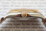Close-up of two-tone luxury watch crown and fluted bezel on a blurred text background