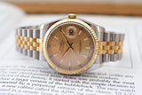 Two-tone luxury watch with gold fluted bezel and champagne dial resting on open book