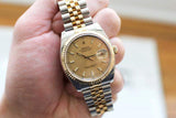 Two-tone gold and steel luxury watch with champagne dial held in hand, showing date display