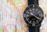 Blancpain Fifty Fathoms luxury dive watch with black strap on a colorful map background