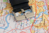 Close-up of a luxury watch black fabric strap with silver clasp on a colorful map