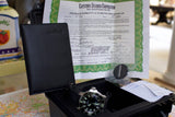 Luxury dive watch with authentication papers, black case, and accessories on table