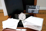 Silver luxury watch with black leather strap in display box, paperwork and authenticity card