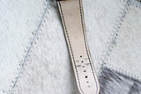 Close-up of light leather watch strap with black stitching on textured white background.