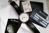 Luxury Blancpain watch with white dial and black leather strap, shown with documents and warranty cards