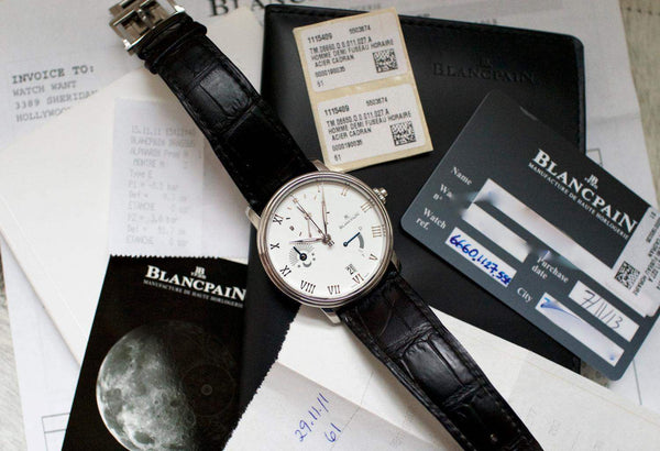 Luxury Blancpain watch with white dial and black leather strap, shown with documents and warranty cards