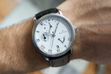 Stainless steel dress watch with white dial, Roman numerals, and leather strap on wrist