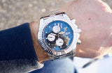 Close-up of a silver Breitling luxury chronograph watch with a blue dial on a wrist.