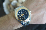 Luxury Swiss automatic watch with blue and gold bezel, silver bracelet, worn on wrist