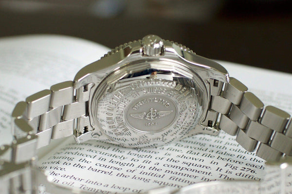 Stainless steel luxury watch back with engraved details and metal bracelet on open book