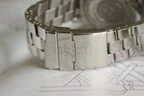 Close-up of stainless steel luxury watch bracelet clasp with engraved logo and fine detailing.