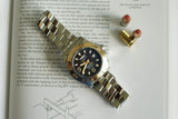 Stainless steel luxury dive watch with black dial on book, next to two bullets
