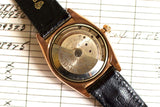 Vintage rose gold automatic watch with black leather strap, open caseback showing movement.