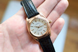 Vintage rose gold Oyster Perpetual watch with black leather strap held in hand