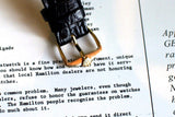 Close-up of a black leather watch strap with gold buckle on vintage document