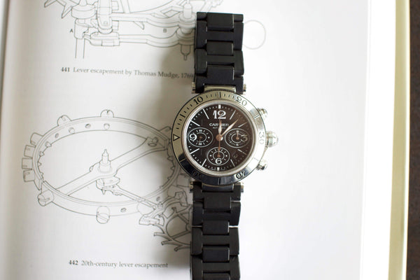 Black chronograph luxury watch with metal bezel and rubber strap on a technical drawing